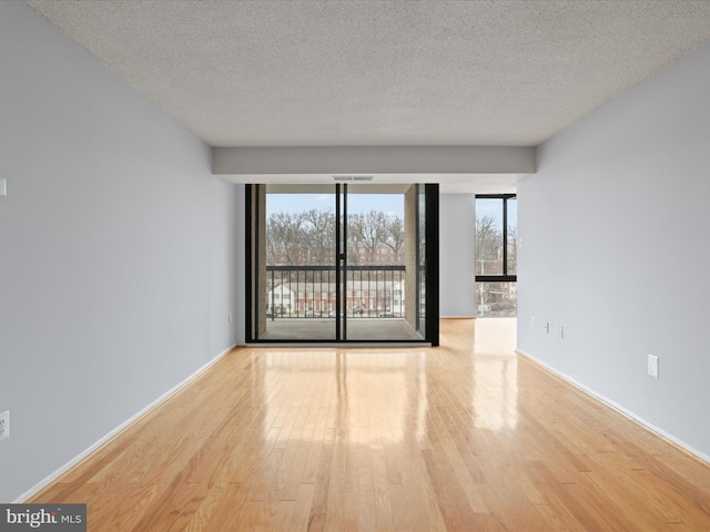 empty room with a wall of windows, a textured ceiling, and wood finished floors