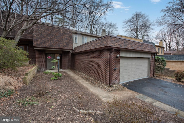 view of front facade featuring mansard roof, an attached garage, a shingled roof, brick siding, and driveway