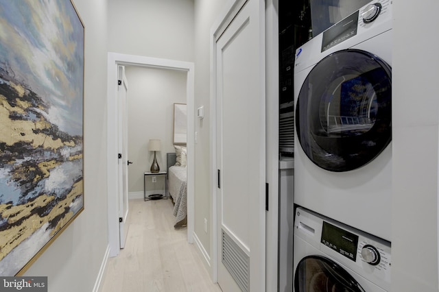 laundry area with stacked washer and clothes dryer, baseboards, light wood finished floors, and laundry area