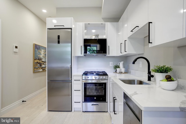 kitchen with light stone counters, appliances with stainless steel finishes, white cabinetry, a sink, and modern cabinets