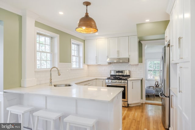 kitchen with a peninsula, a sink, stainless steel appliances, white cabinets, and under cabinet range hood