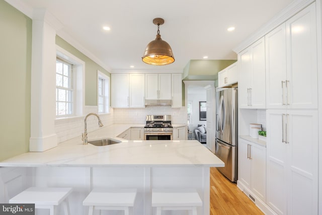 kitchen with a peninsula, a sink, stainless steel appliances, white cabinets, and backsplash