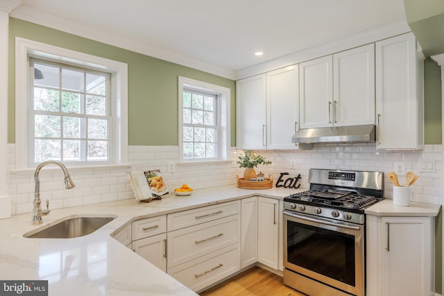 kitchen with light stone counters, a sink, white cabinets, under cabinet range hood, and stainless steel gas stove