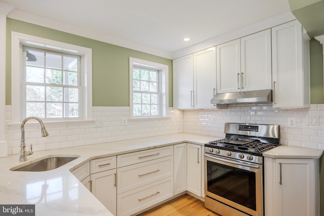 kitchen featuring light stone countertops, under cabinet range hood, gas stove, white cabinetry, and a sink