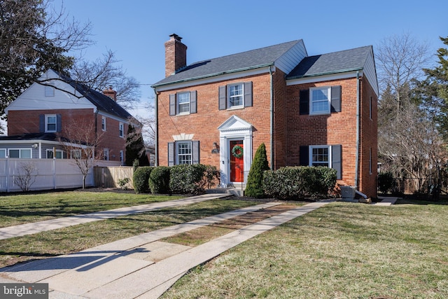 colonial inspired home with a front lawn, brick siding, a chimney, and fence