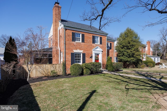 view of front of house with brick siding, a chimney, a front yard, and fence