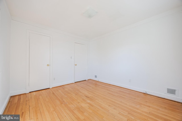 empty room with hardwood / wood-style flooring, crown molding, visible vents, and baseboards