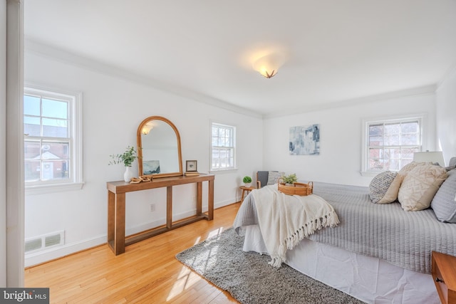 bedroom with light wood finished floors, visible vents, baseboards, and ornamental molding