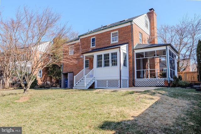 back of house featuring a lawn, brick siding, a sunroom, and a chimney