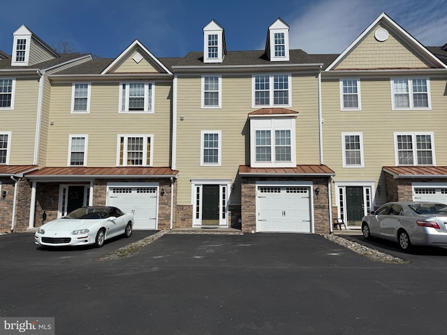 townhome / multi-family property with stone siding, an attached garage, driveway, and a standing seam roof