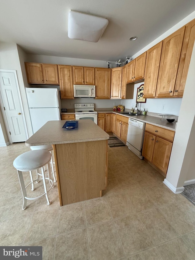 kitchen featuring white appliances, a sink, a kitchen island, baseboards, and a kitchen bar