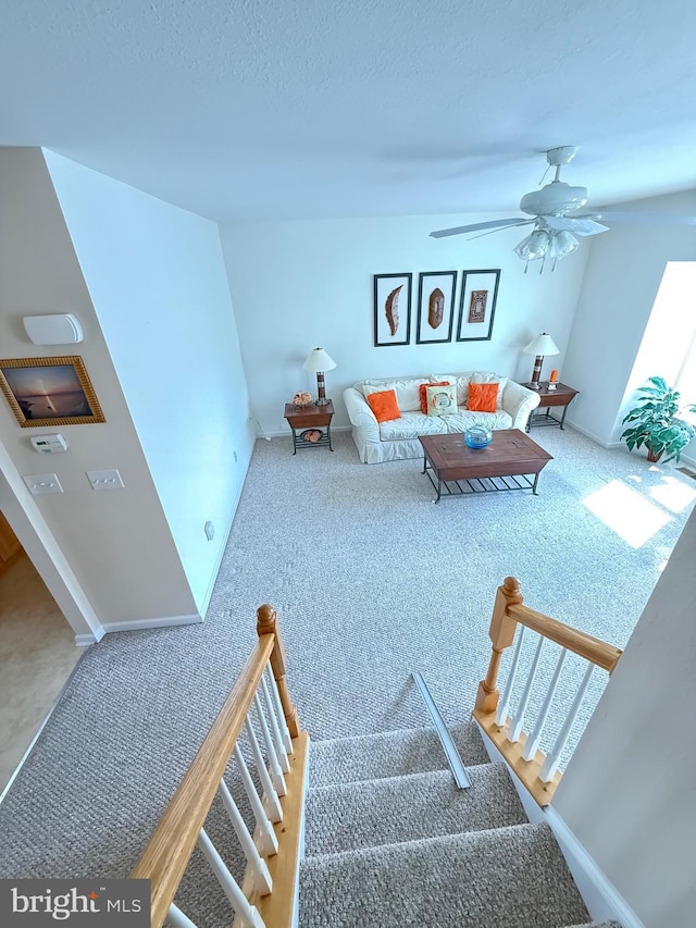 carpeted living room with ceiling fan, stairway, a textured ceiling, and baseboards