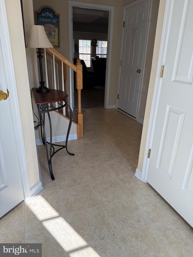 corridor featuring stairs, baseboards, and light tile patterned floors