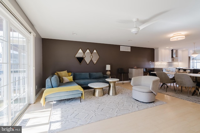 living room featuring a wealth of natural light, visible vents, a ceiling fan, and light wood finished floors