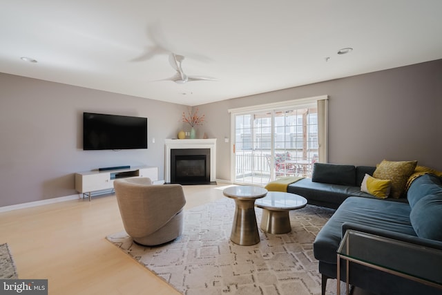 living area with a ceiling fan, a glass covered fireplace, recessed lighting, light wood finished floors, and baseboards