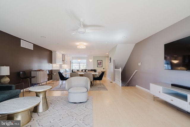 living room featuring a ceiling fan, baseboards, visible vents, and light wood-type flooring