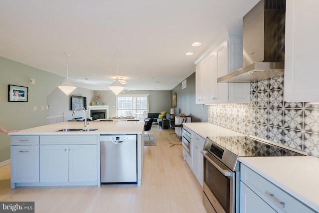 kitchen featuring open floor plan, decorative backsplash, appliances with stainless steel finishes, wall chimney exhaust hood, and a sink