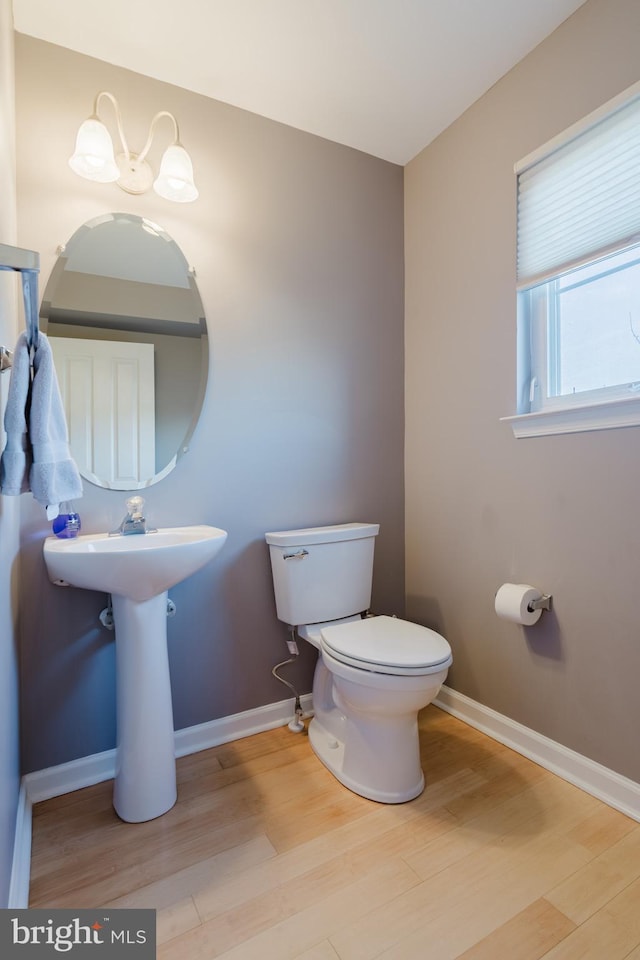 half bathroom featuring toilet, baseboards, and wood finished floors