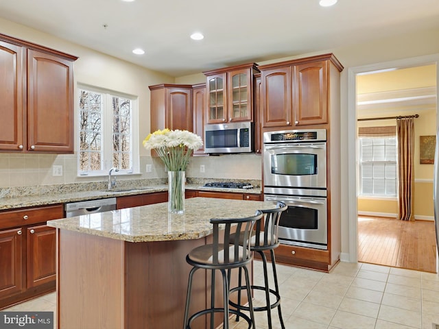 kitchen featuring light tile patterned floors, light stone counters, appliances with stainless steel finishes, a sink, and backsplash