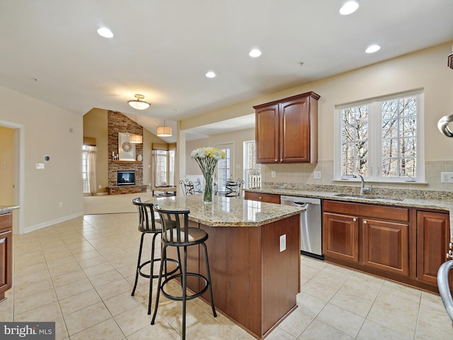 kitchen with light stone counters, a fireplace, vaulted ceiling, a sink, and dishwasher