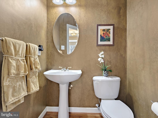 half bath with a sink, wood finished floors, toilet, and baseboards