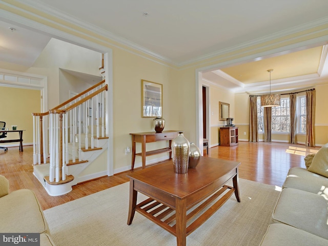 living area with baseboards, light wood-style floors, ornamental molding, stairway, and a raised ceiling