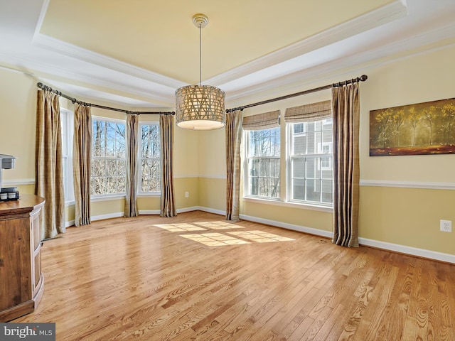 unfurnished dining area with ornamental molding, a tray ceiling, and light wood-style flooring