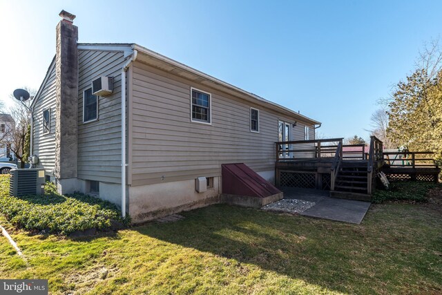 rear view of house with a wooden deck, a wall mounted air conditioner, central AC unit, a chimney, and a yard