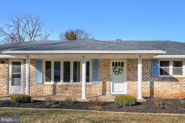 property entrance featuring brick siding, a porch, and a shingled roof