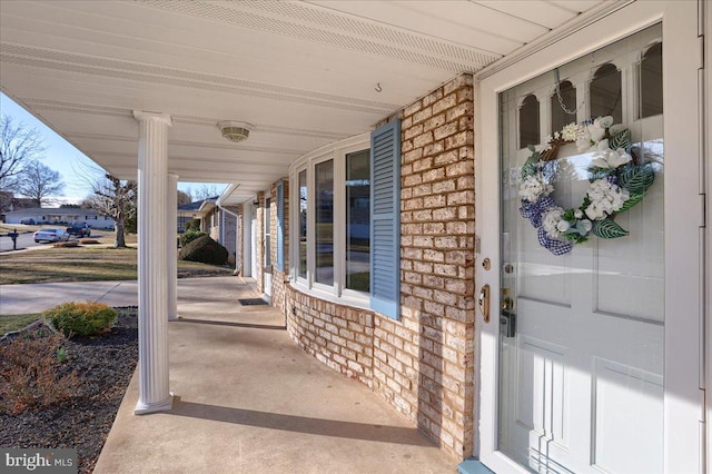 entrance to property featuring a porch and brick siding