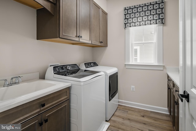 clothes washing area with light wood-style flooring, a sink, baseboards, washer and dryer, and cabinet space