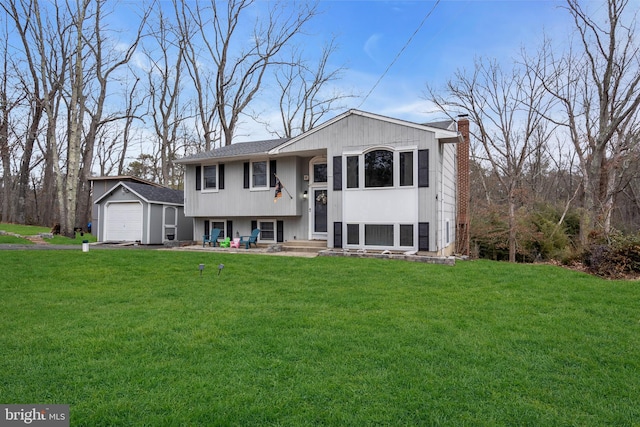 bi-level home featuring a chimney, a front lawn, a detached garage, and an outbuilding