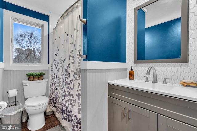 bathroom featuring toilet, wood finished floors, vanity, wainscoting, and decorative backsplash