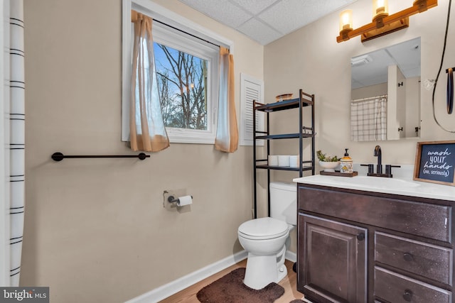 full bathroom featuring a paneled ceiling, baseboards, toilet, and vanity