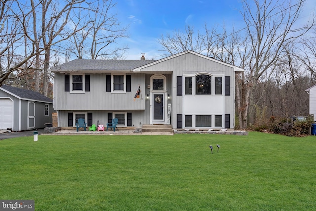 raised ranch featuring an outbuilding, roof with shingles, a front lawn, and a chimney