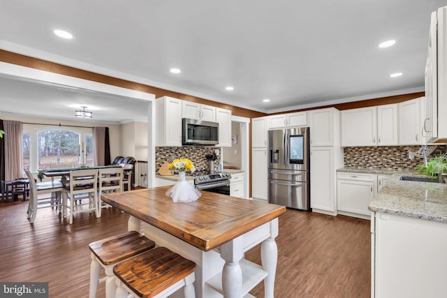 kitchen with light stone counters, stainless steel appliances, dark wood-type flooring, a sink, and white cabinetry