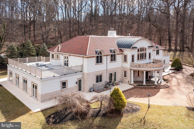 back of house featuring a balcony, a chimney, metal roof, and a yard