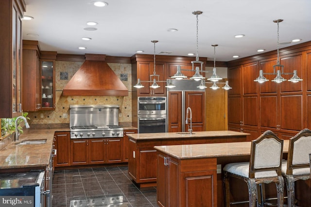 kitchen featuring a center island with sink, custom exhaust hood, decorative backsplash, stainless steel double oven, and a sink