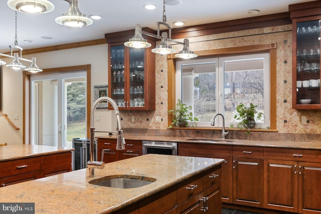 kitchen with hanging light fixtures, light stone countertops, decorative backsplash, and a sink