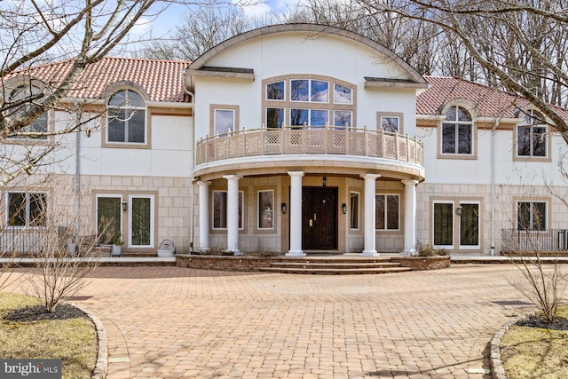 view of front of house featuring a balcony, a tile roof, and stucco siding