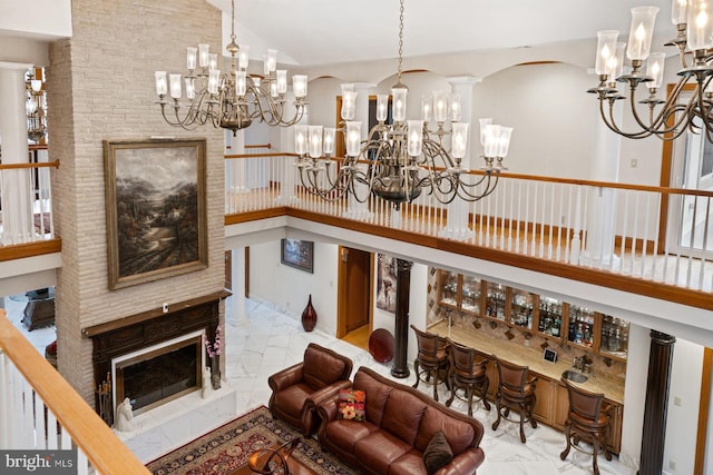 bar with marble finish floor, high vaulted ceiling, a notable chandelier, and a glass covered fireplace