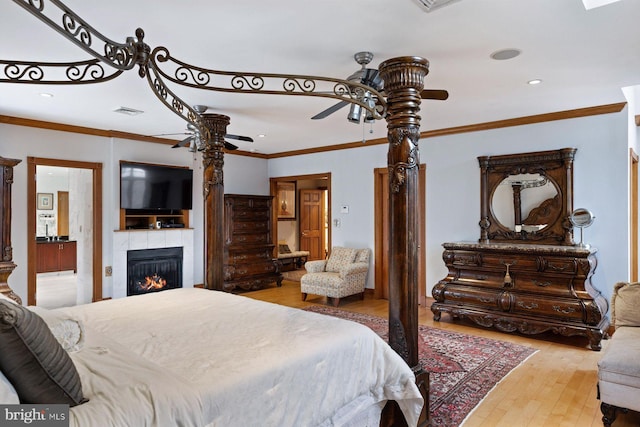 bedroom featuring visible vents, a tile fireplace, wood-type flooring, ceiling fan, and ornamental molding