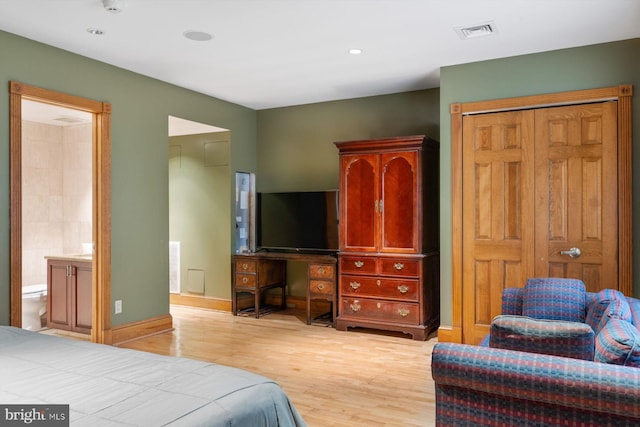 bedroom with a closet, visible vents, ensuite bath, light wood-type flooring, and baseboards