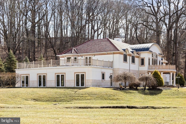 rear view of house featuring a balcony, a chimney, a lawn, and a tiled roof