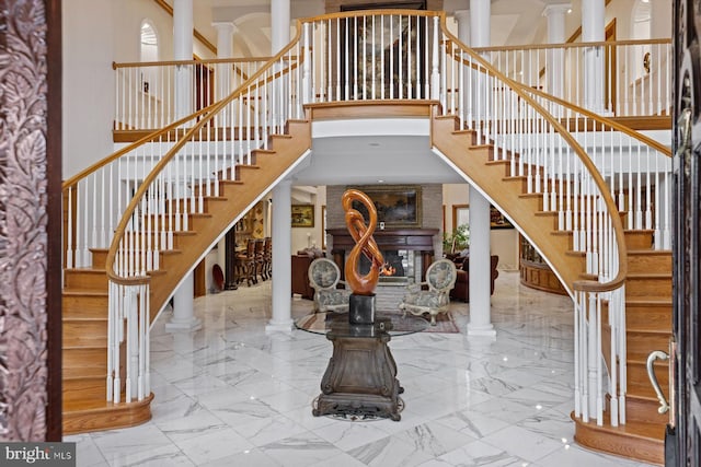 foyer with a large fireplace, a towering ceiling, stairs, marble finish floor, and decorative columns