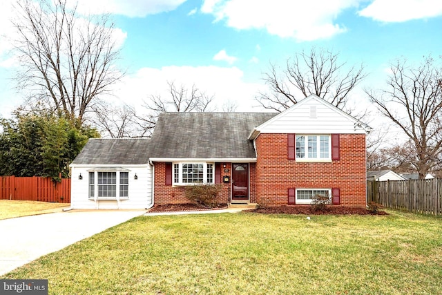 tri-level home featuring driveway, brick siding, a front yard, and fence