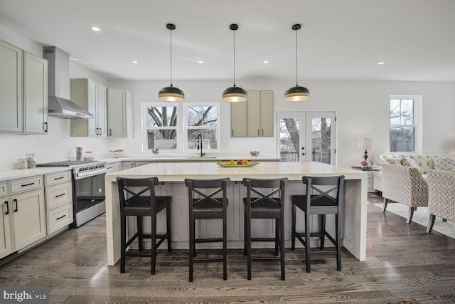 kitchen with stainless steel gas range oven, a kitchen breakfast bar, light countertops, and wall chimney range hood