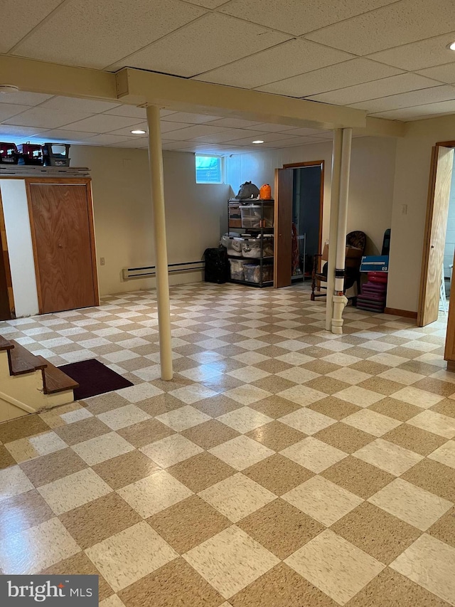 basement featuring light floors, a drop ceiling, and baseboards