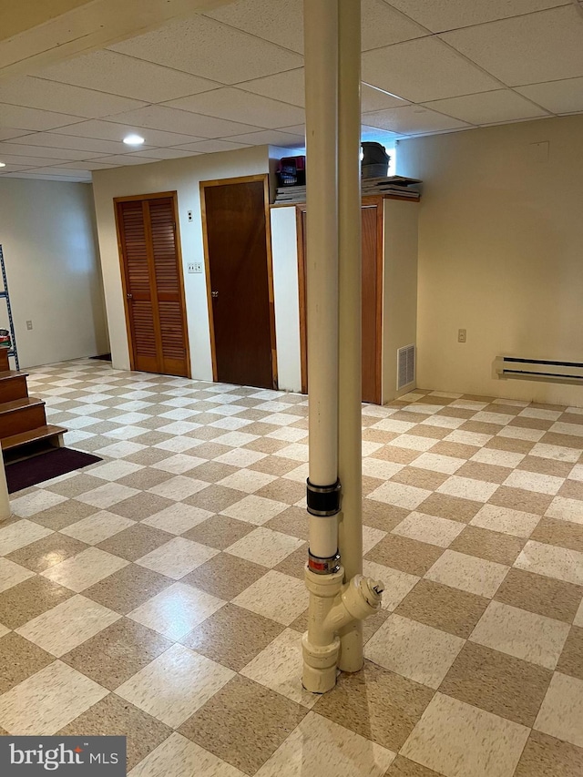 finished basement featuring a baseboard heating unit, a paneled ceiling, and visible vents