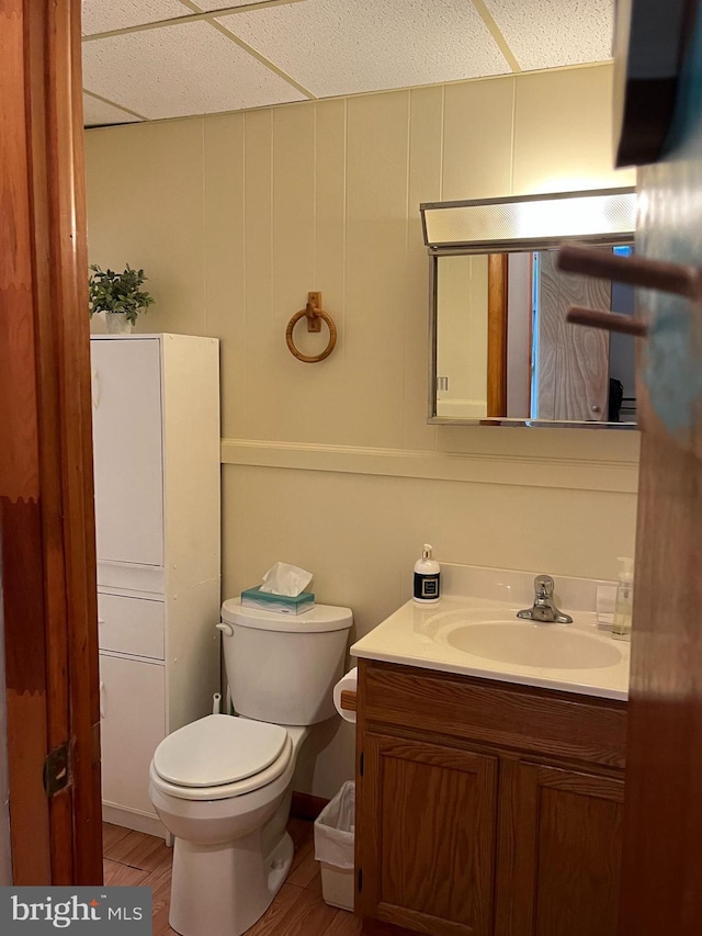 half bath featuring toilet, wood finished floors, a drop ceiling, and vanity